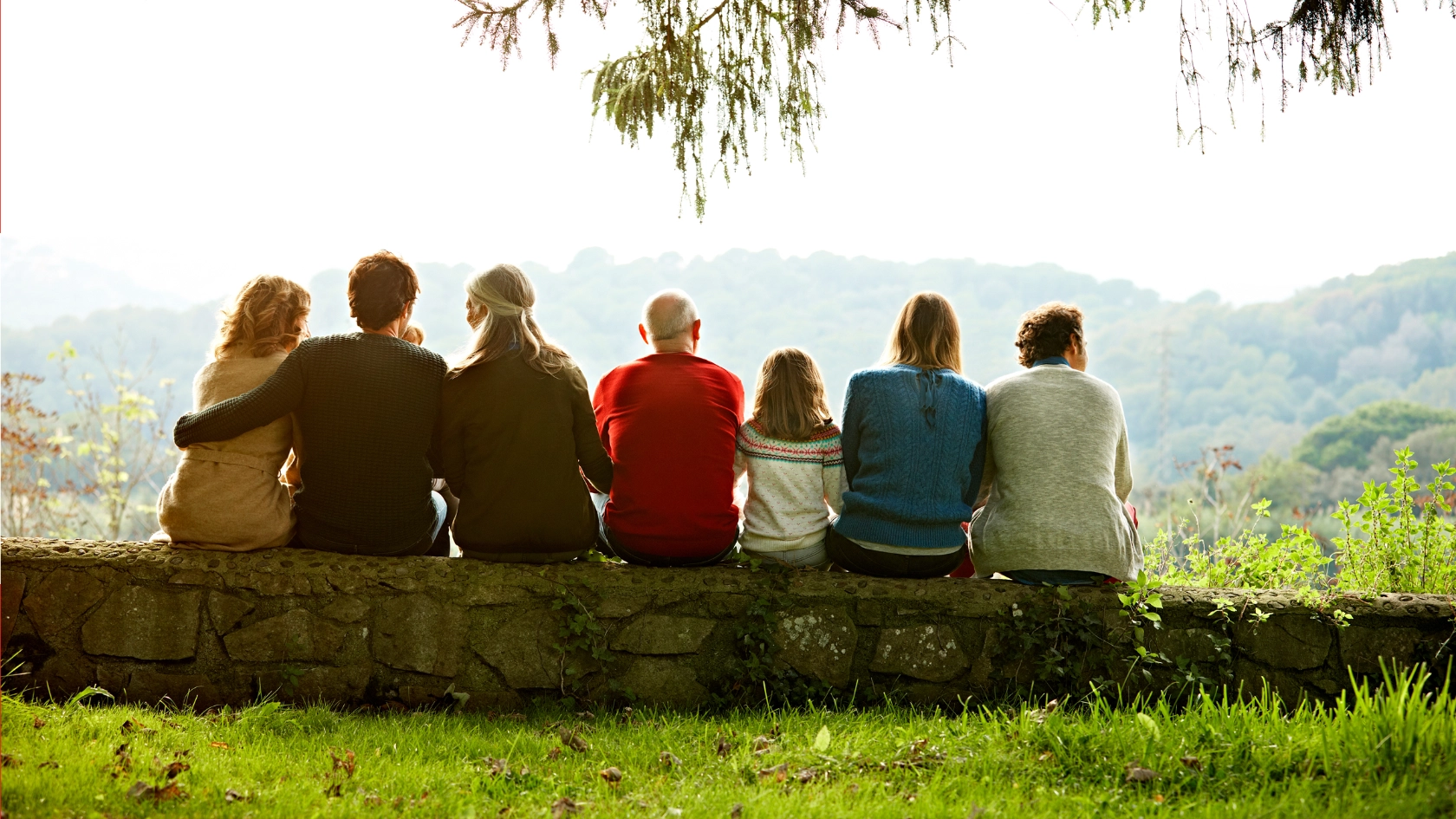 Mehrere Personen verschiedener Generationen sitzen auf einer Mauer.
