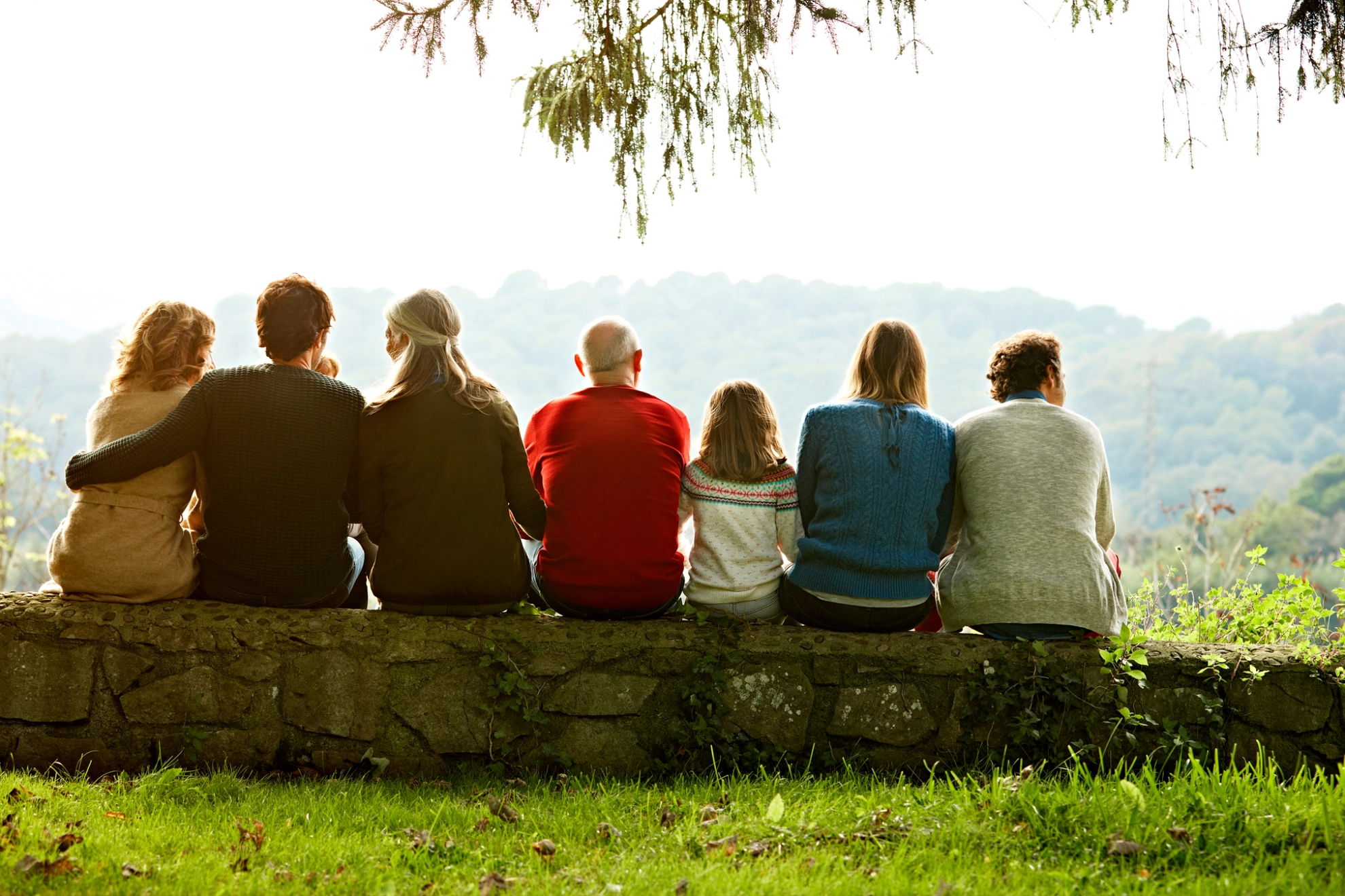 Mehrere Personen verschiedener Generationen sitzen auf einer Mauer.