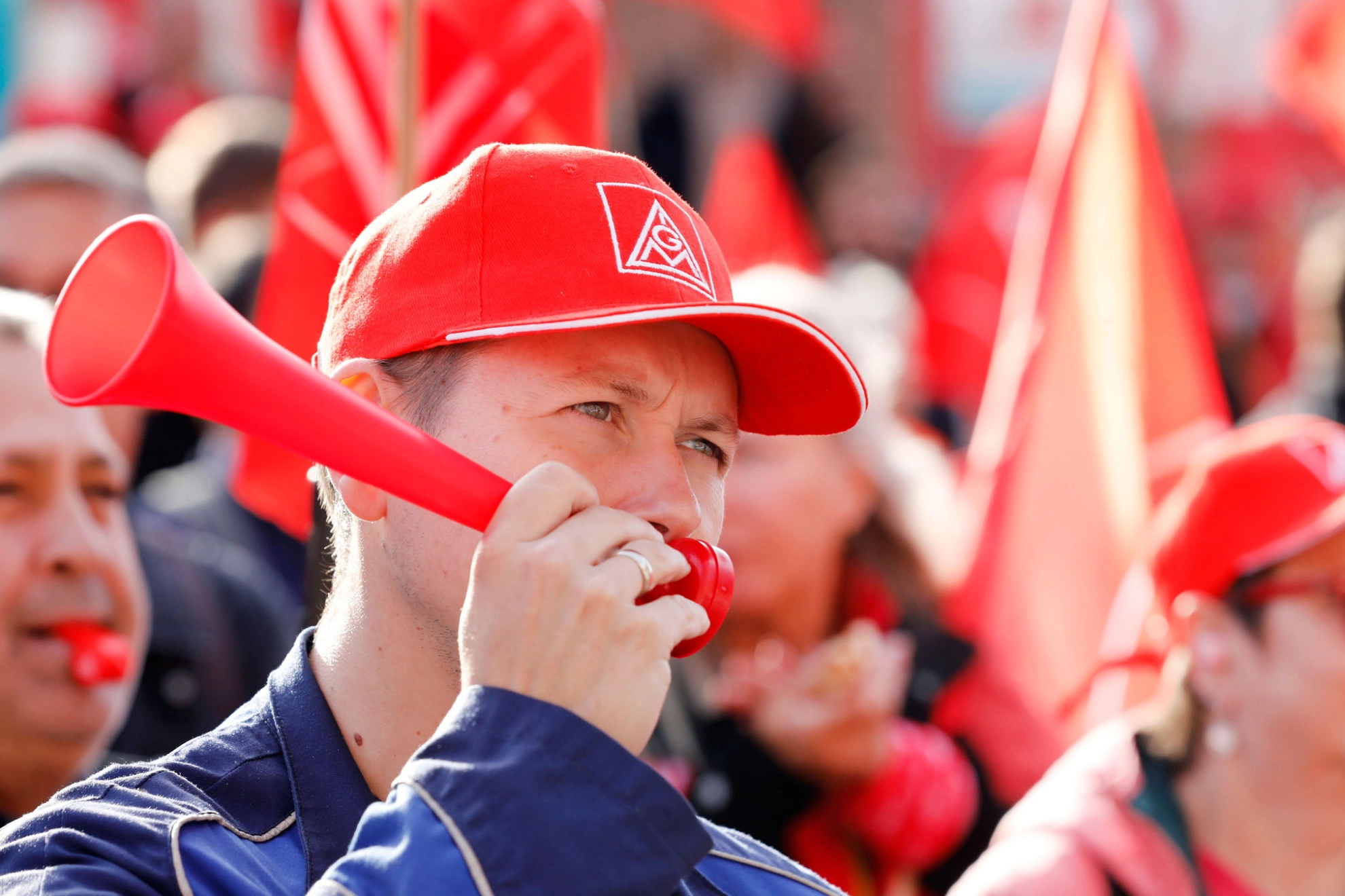 Ein Mann mit IG Metall-Kappe und Signaltröte in einer Menschenmenge