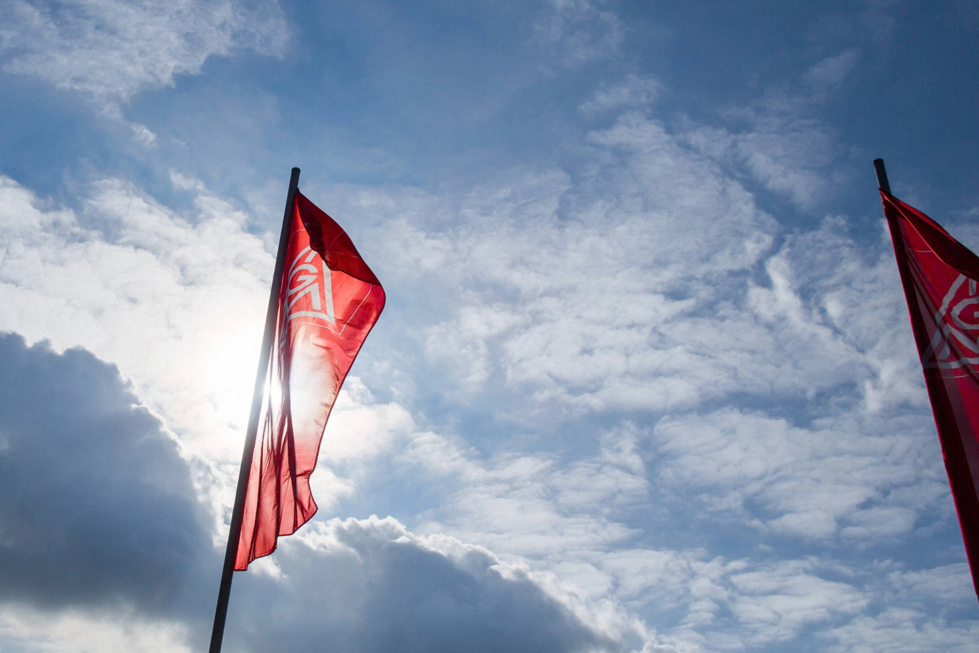 IG Metall-Fahnen vor leicht bewölktem Himmel.